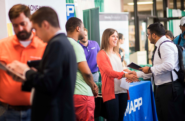 Students in professional dress meet with tabling representatives at a College of Engineering career fair