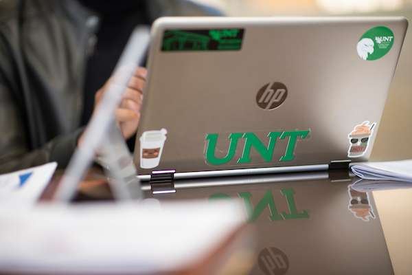 An open laptop decorated with UNT stickers