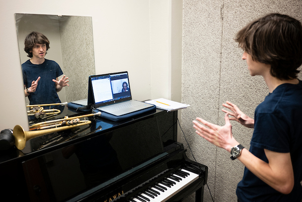 A piano and French horn instructor gives a virtual music lesson to a student over a laptop