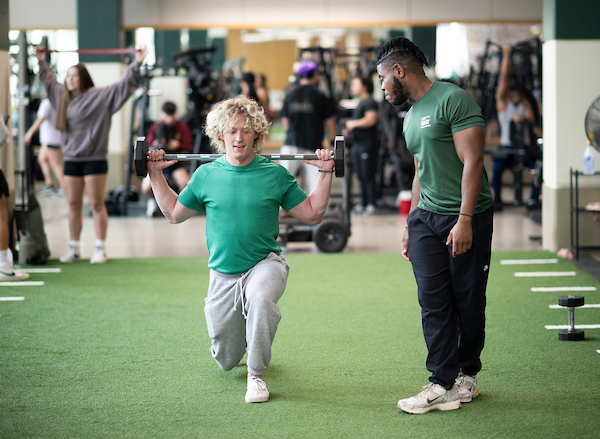 A student accompanied by a trainer does lunges with a barbell at the Pohl Rec Center 