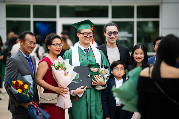 A student poses with his family and diploma at commencement
