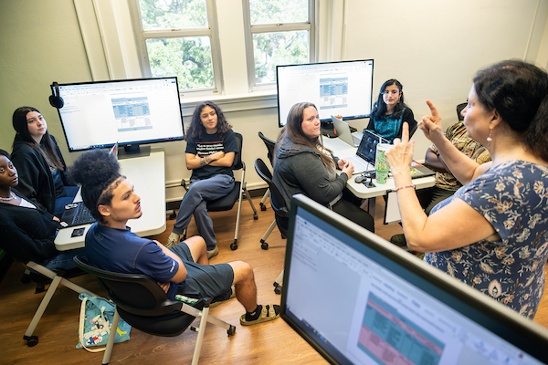 Students working in groups listen to an instructor in a data analytics clas