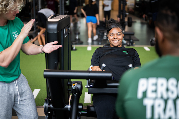 A student uses a leg press weight machine at the Pohl Rec Center overseen by a trainer
