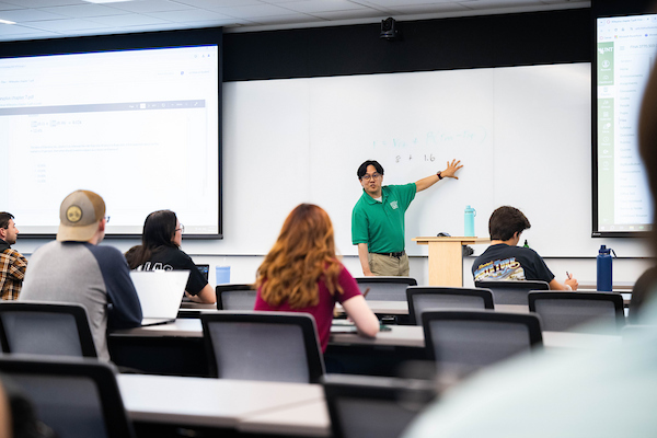 A faculty presents at a whiteboard in front of a class