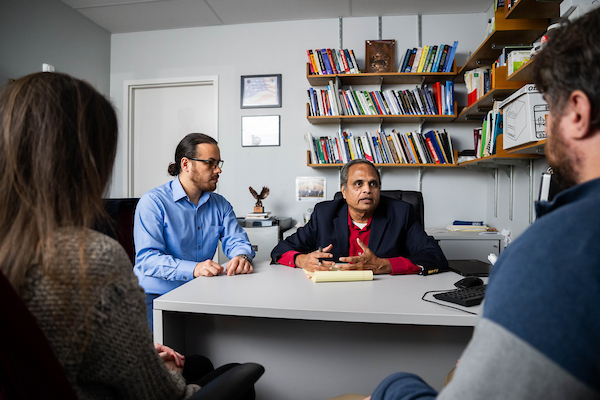 A faculty member meets with students and a graduate assistant in his office