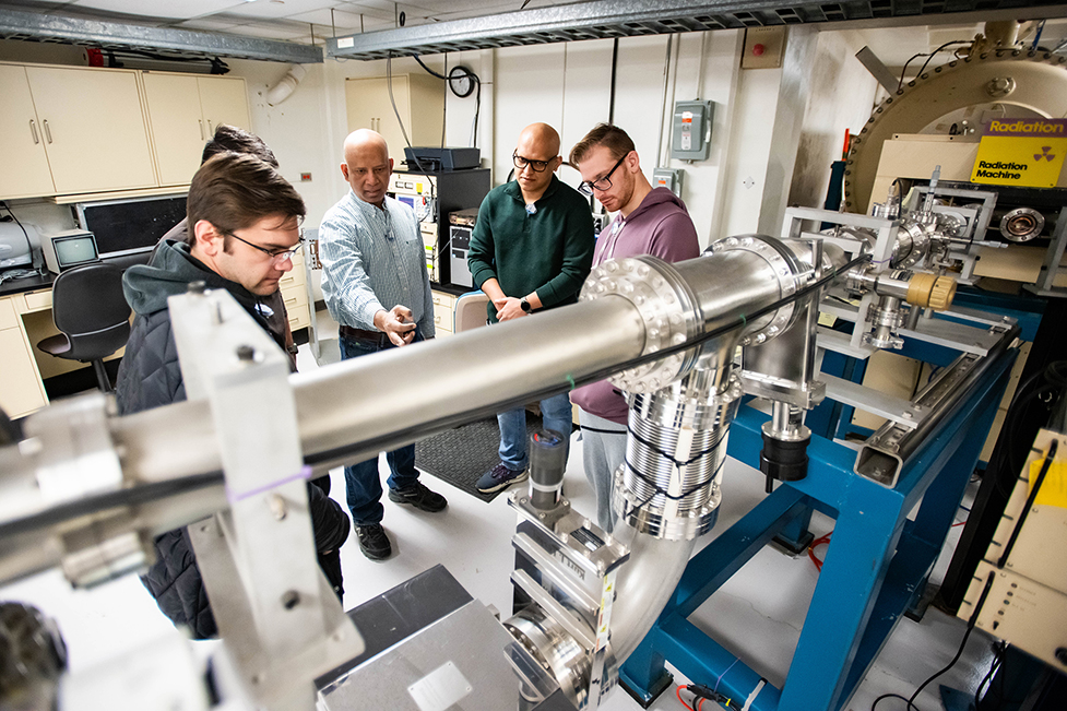 UNT researchers have a discussion near an ion accelerator, which is being used to conduct radiation ground testing on solar cells.