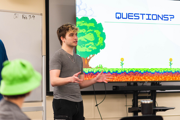 A student gives a game studies presentation with an 8-bit style PowerPoint slide deck
