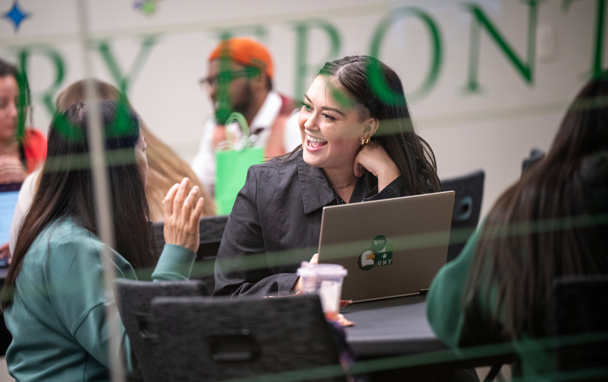 Two students chatting while working at their laptops