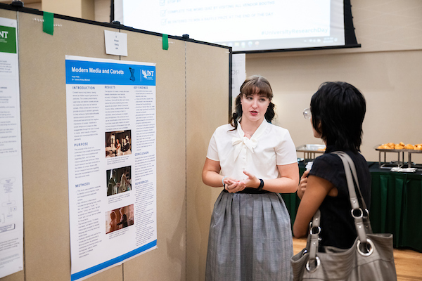 Two students discuss a media studies research poster at a symposium