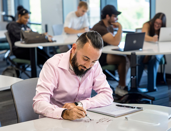 A student takes notes on a whiteboard desk in class