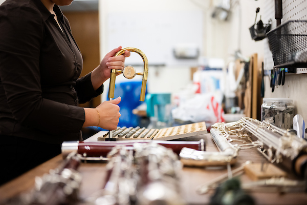 A student works with a brass instrument's parts in a workshop setting