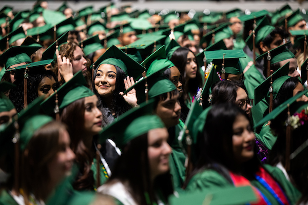 Students in green regalia prepare to walk the stage at commencement