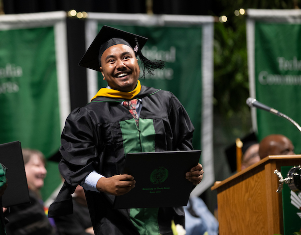 A student smiles while holding his diploma at commencement